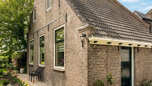 A brick house with a tiled roof, a covered patio with chairs, and a garden with flowers. - Cozy home in Harich with WiFi (Harich)