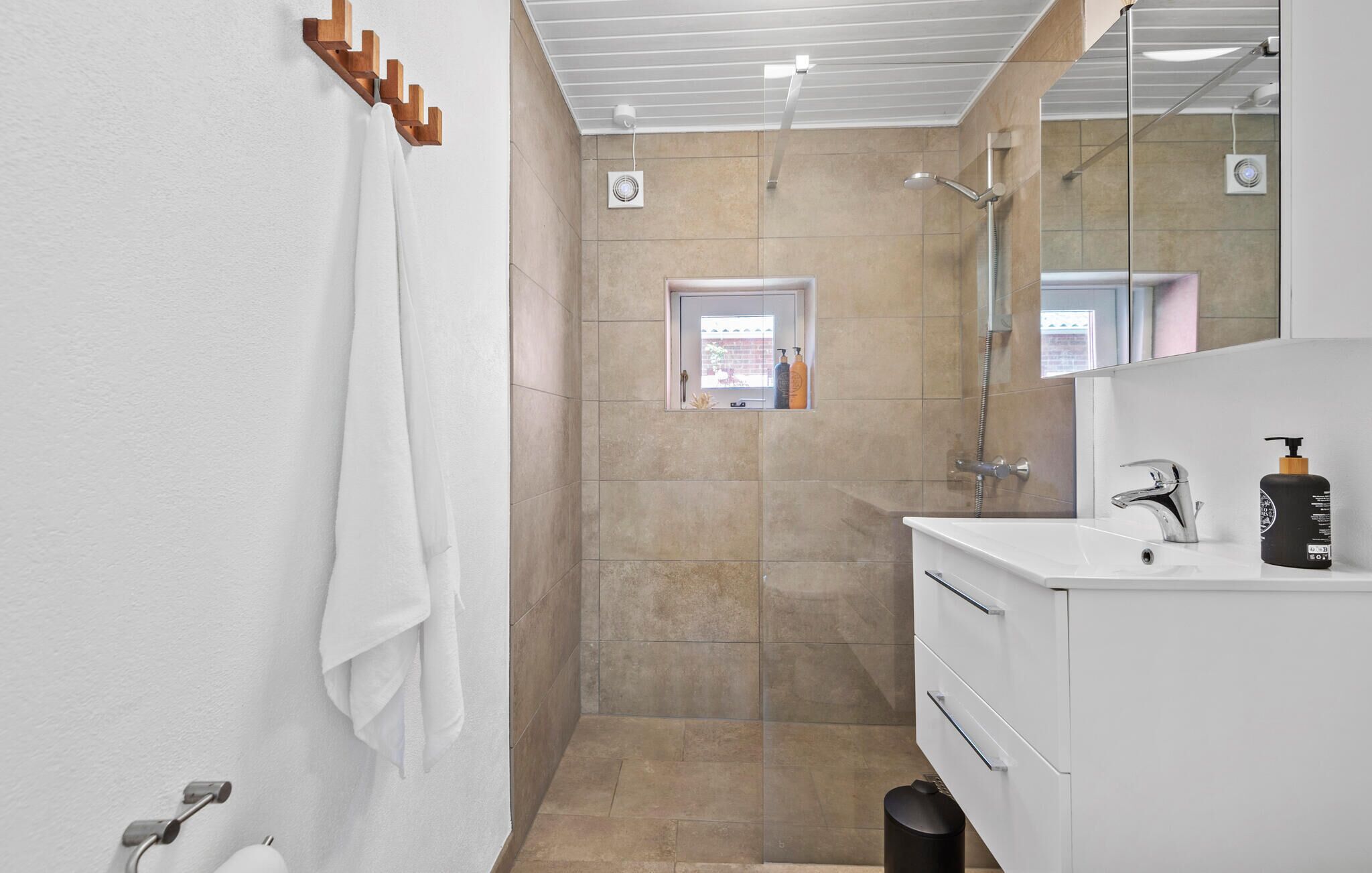 A modern bathroom with a shower, a sink, and a mirror. There is a towel rack on the wall and a small window above the shower.