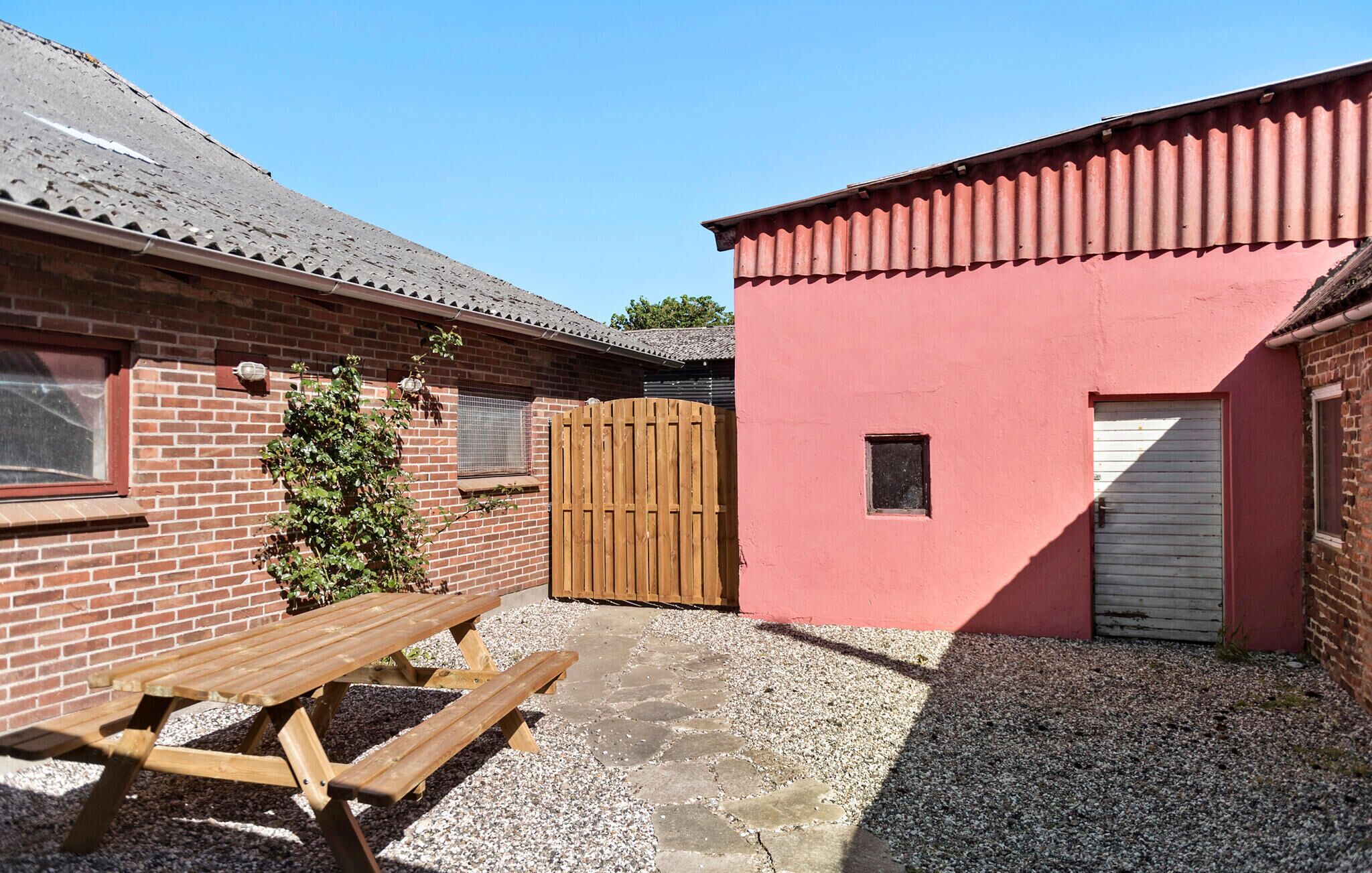 Een binnenplaats met een picknicktafel, een houten poort en een rood gebouw met een garagedeur.