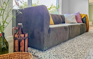 A modern living room with a grey sofa, a woven basket, and a wooden bottle stand.