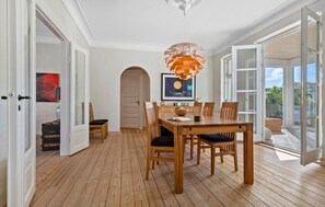 A dining area with a wooden table and chairs, a modern pendant light, and a large window with a view of the outdoors. - Nice home in Løgstør with WiFi (Løgstør)