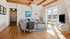 A spacious loft apartment with a high wooden ceiling, a large window offering a view of the city, a modern sofa, a coffee table, and a flat-screen TV. - Nice home in Løgstør with WiFi (Løgstør)