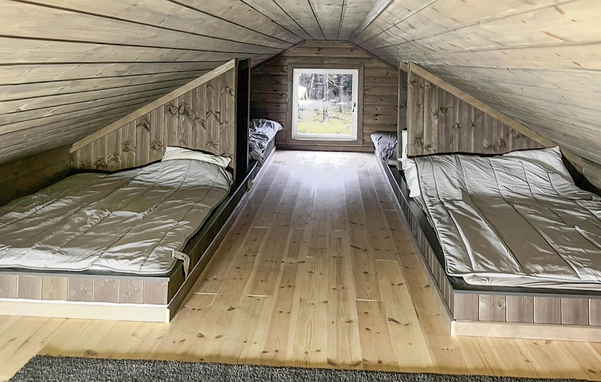 A small attic bedroom with two single beds, wooden walls, and a window providing a view of the outdoors.
