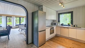 Une cuisine moderne équipée d’un réfrigérateur, d’un four à micro-ondes, d’un four et d’un lave-vaisselle. Un coin repas est aménagé avec une chaise et une table.