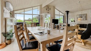 A spacious dining area with a wooden table and chairs, large windows offering a view of greenery, and a cozy seating area with a fireplace.