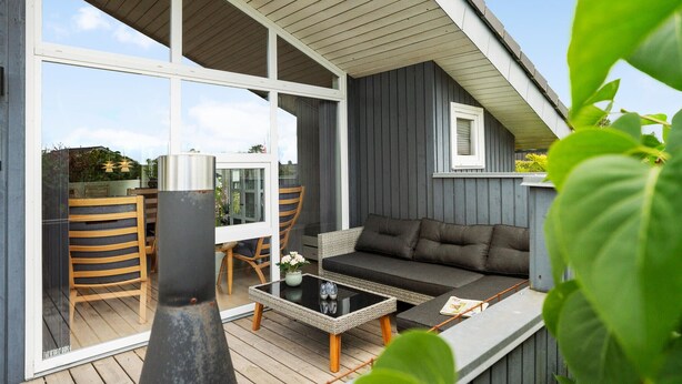 A modern outdoor seating area with a glass partition, wicker furniture, and a wooden deck.