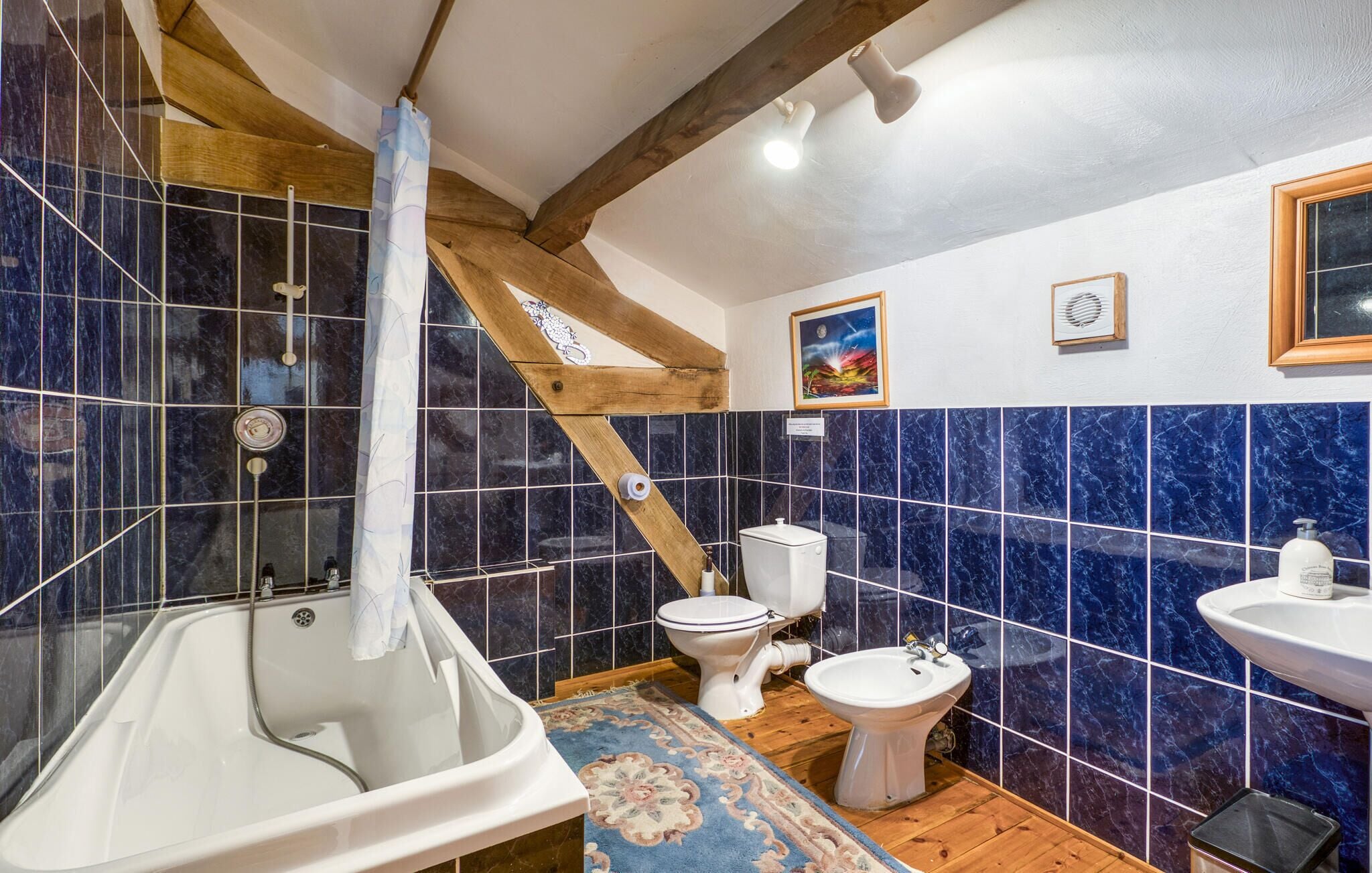 A bathroom with a bathtub, toilet, bidet, and sink, featuring blue marble tiles and wooden beams.