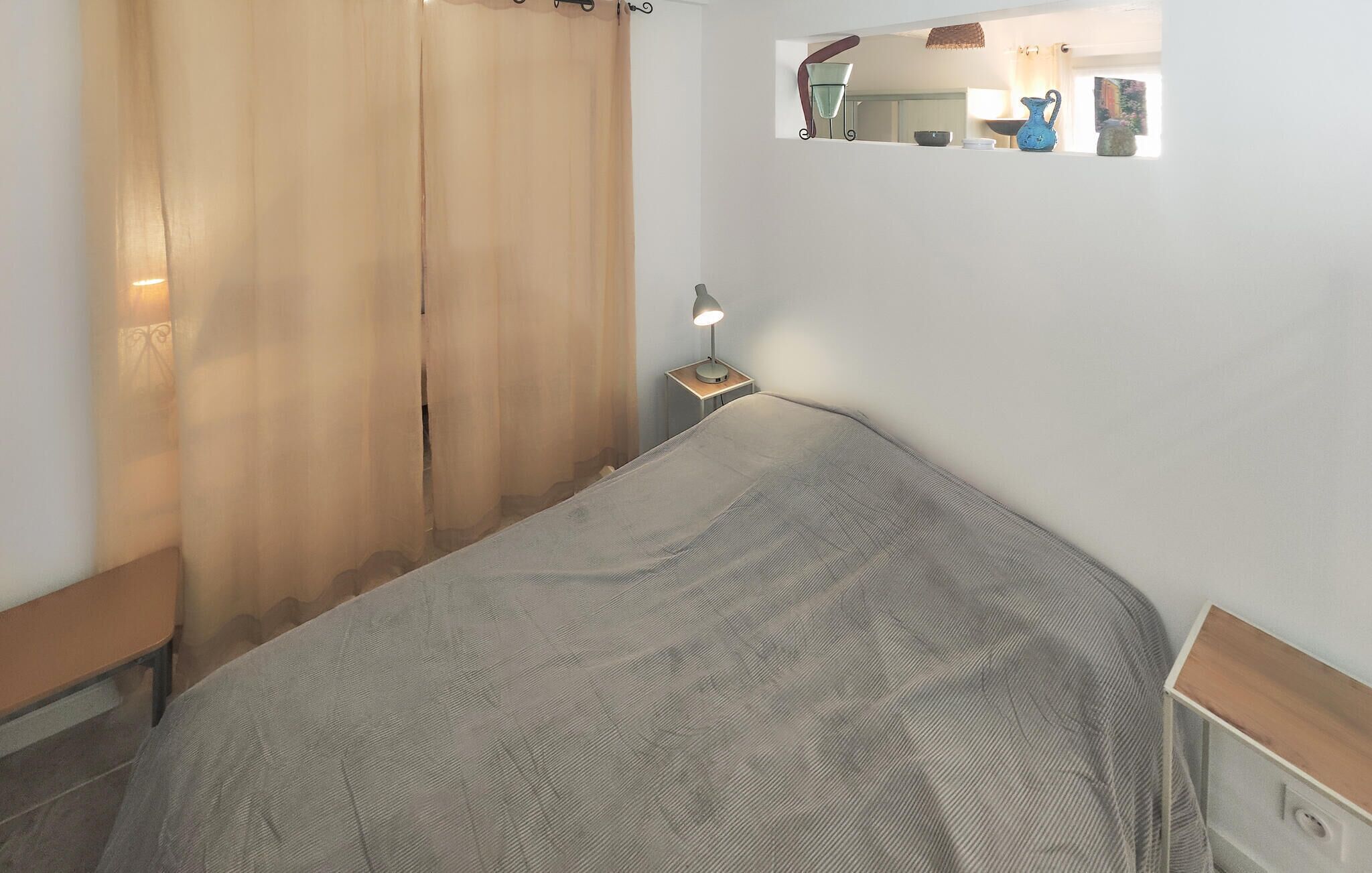 A bedroom with a bed, a nightstand with a lamp, a mirror, and a window with curtains.