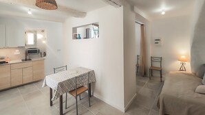 Een ruimtelijk ingerichte leefruimte met kitchenette, een eethoek met tafel en stoelen, een bed en een kleine badkamer.
