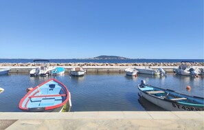 A marina with several boats docked, a rocky shoreline, and a clear view of the sea.