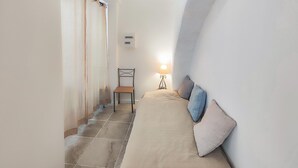 Een smalle gang met een bed, een stoel en een lamp.