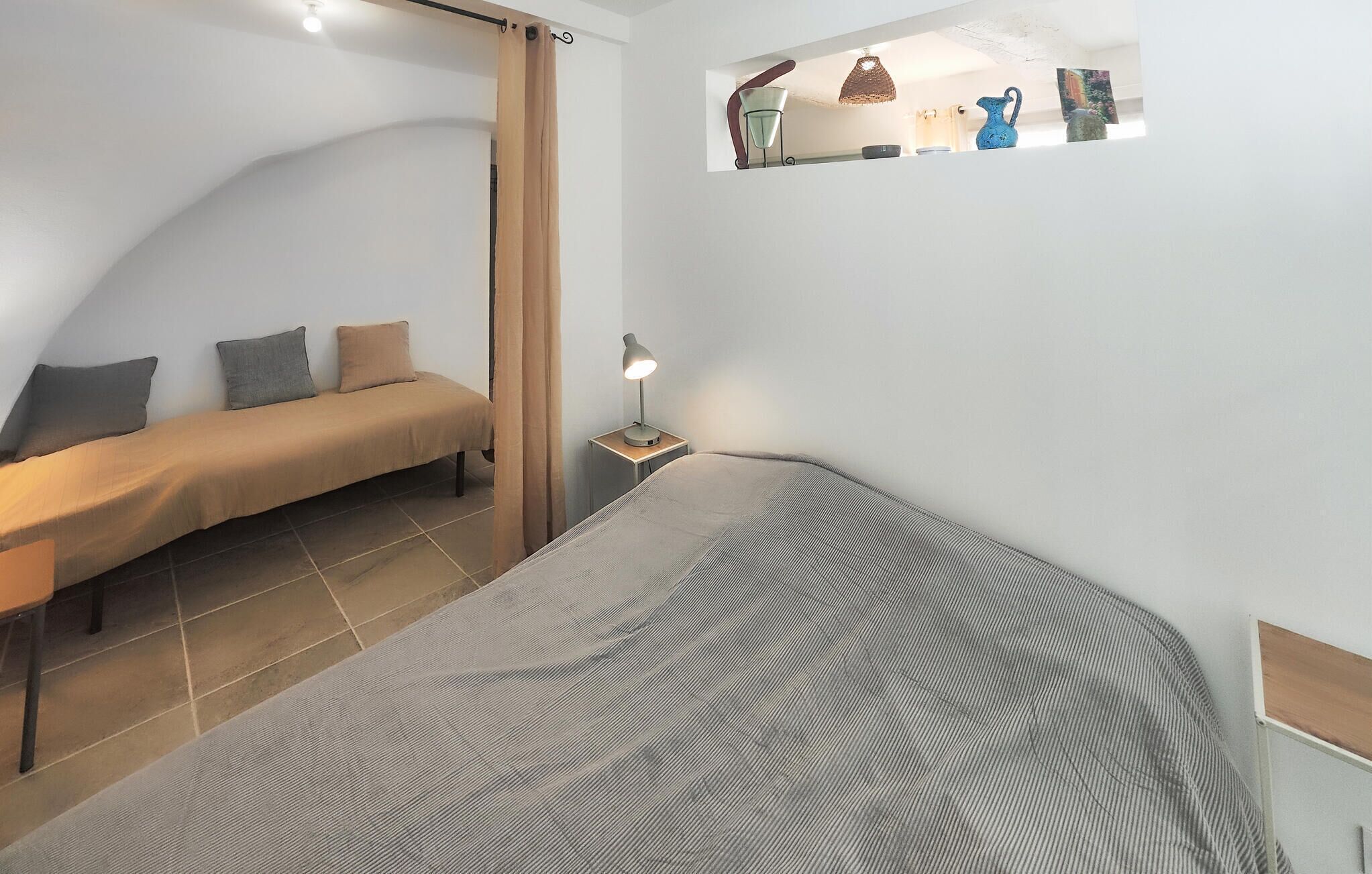 A bedroom with a bed, a nightstand, a lamp, and a shelf with decorative items.