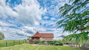 A stone house with a red roof, surrounded by a well-maintained lawn and a wooden fence. - Superbe maison piscine privée (Payzac)