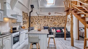 A rustic interior with a stone wall, wooden staircase, and a cozy seating area. - Superbe maison piscine privée (Payzac)