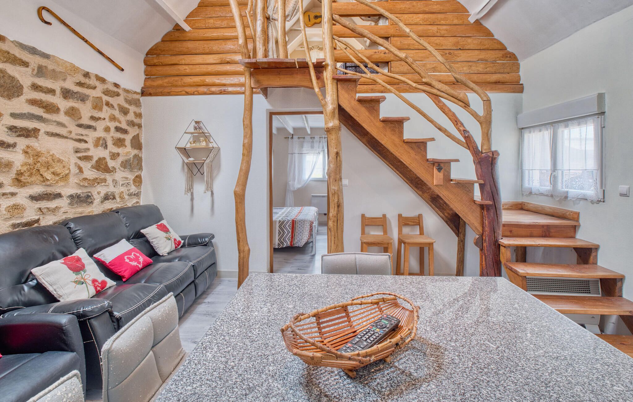 Una habitación acogedora con pared de piedra, un sofá de cuero negro, una escalera de madera y una cesta tejida sobre una mesa de granito.