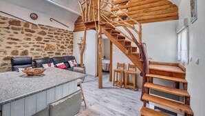 A rustic interior with a stone wall, a wooden staircase, a leather sofa, and a dining area. - Superbe maison piscine privée (Payzac)