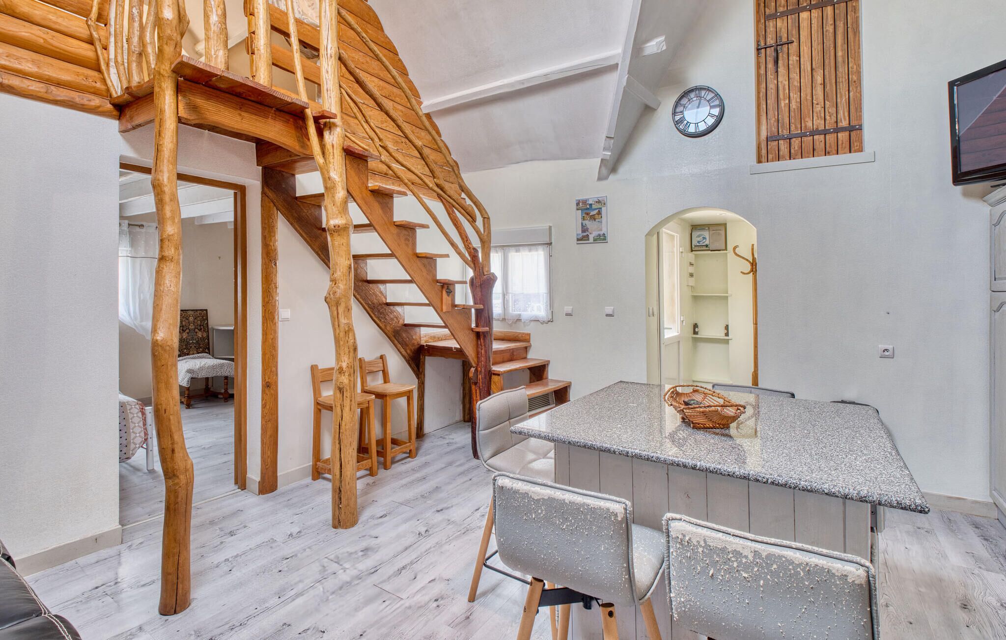 Een ruime kamer met een houten trap, een eethoek met een tafel en stoelen, en een klok aan de muur.