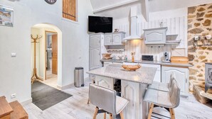 A spacious kitchen with white cabinetry, a central island, and a stone accent wall. - Superbe maison piscine privée (Payzac)