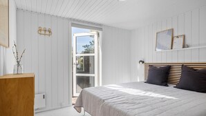 A bedroom with a bed, wooden headboard, and a window with a view of trees.