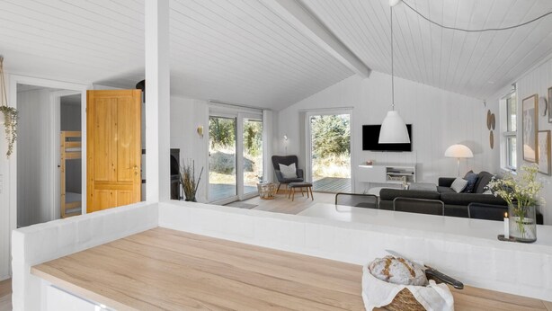 A spacious living area with a wooden floor, a sofa, a dining table, and a kitchen area with a TV.