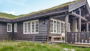 Tunnelmallinen, maalaishenkinen puumökki, jossa on kalteva katto, suuret ikkunat ja kuisti, jossa on puinen kaide.