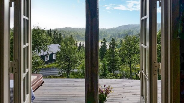 Avoimet puuovet johtavat terassille, jolta avautuu näkymä taloon ja metsäisiin kukkuloihin.