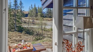 Ruokapöytä, jonka päällä on ruokaa ja juomia, näkymä metsäiselle alueelle ja ikkuna, jossa on koristeellinen kasvi.