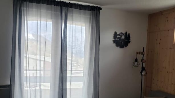 A room with a bed, a small table, a lamp, and a window with sheer curtains. - Apartamento en les Deux Alpes (Les Deux Alpes)