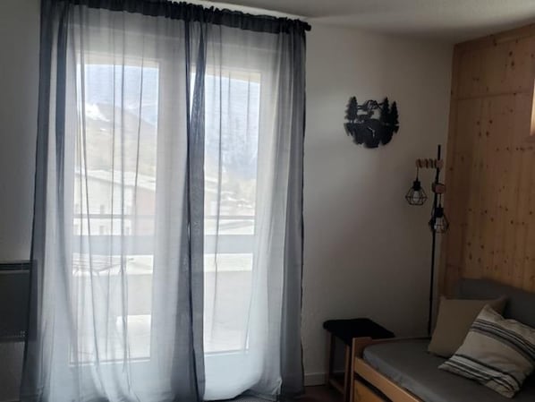 A room with a bed, a small table, a lamp, and a window with sheer curtains. - Apartamento en les Deux Alpes (Les Deux Alpes)