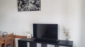 A modern living room with a black entertainment unit, a flat-screen TV, a wooden dining table with chairs, and a black and white abstract painting on the wall. - Apartamento en les Deux Alpes (Les Deux Alpes)