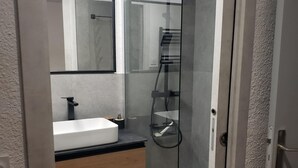 A modern bathroom with a white sink, wooden drawers, a glass shower enclosure, and a mirror above the sink. - Apartamento en les Deux Alpes (Les Deux Alpes)