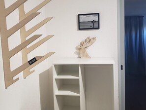 Una estantería blanca con un detalle de madera decorativa en la parte superior, una fotografía enmarcada en la pared y un cortinero azul que se ve parcialmente.