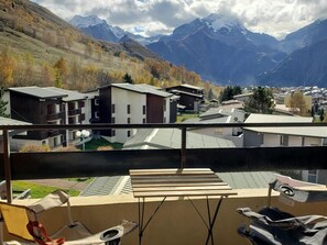 A balcony with a view of a mountain range, modern buildings, and a wooden table.