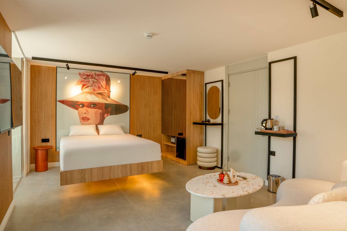 A modern hotel room with a large bed, a round coffee table, a sofa, and a wall-mounted TV.