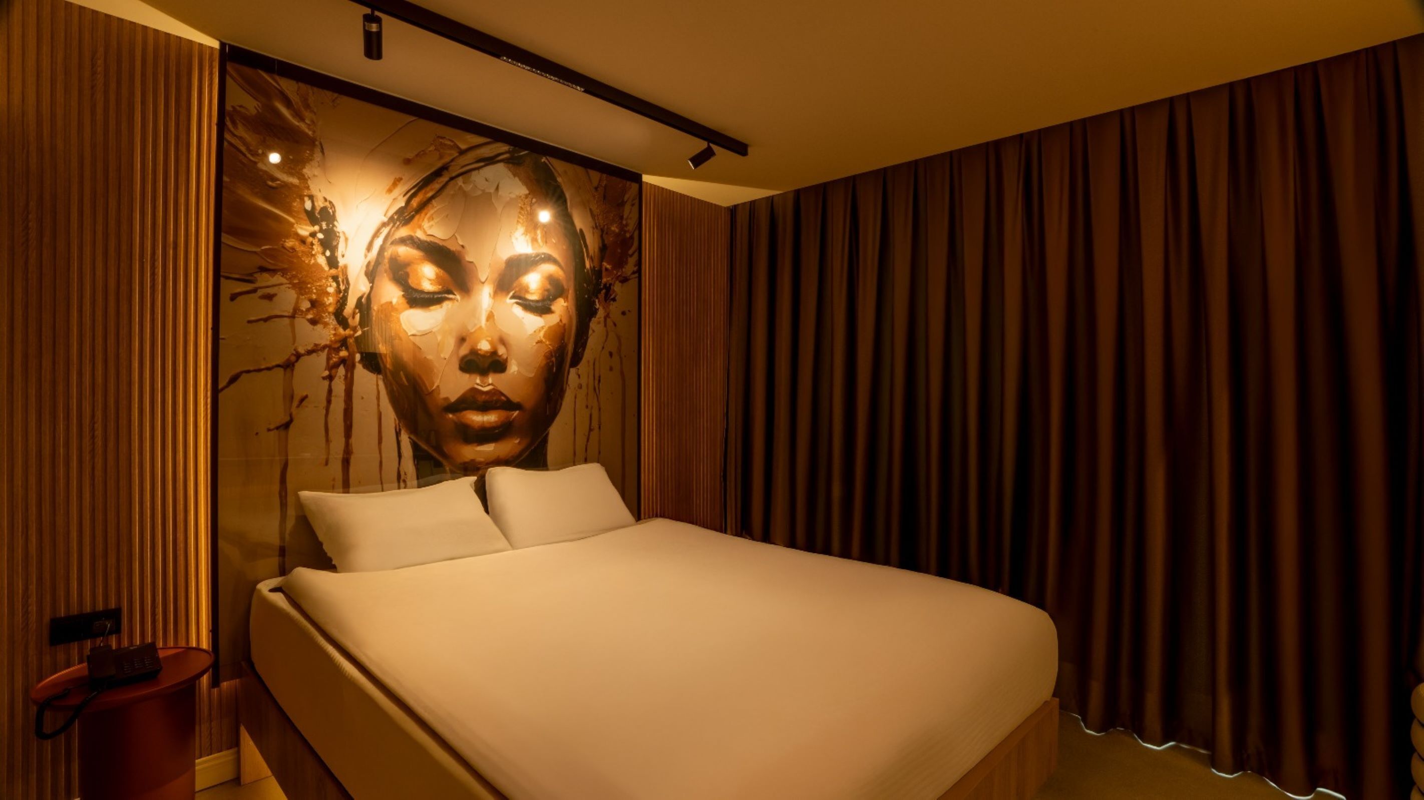 A modern hotel room with a large bed, a wall mural, and a curtain.