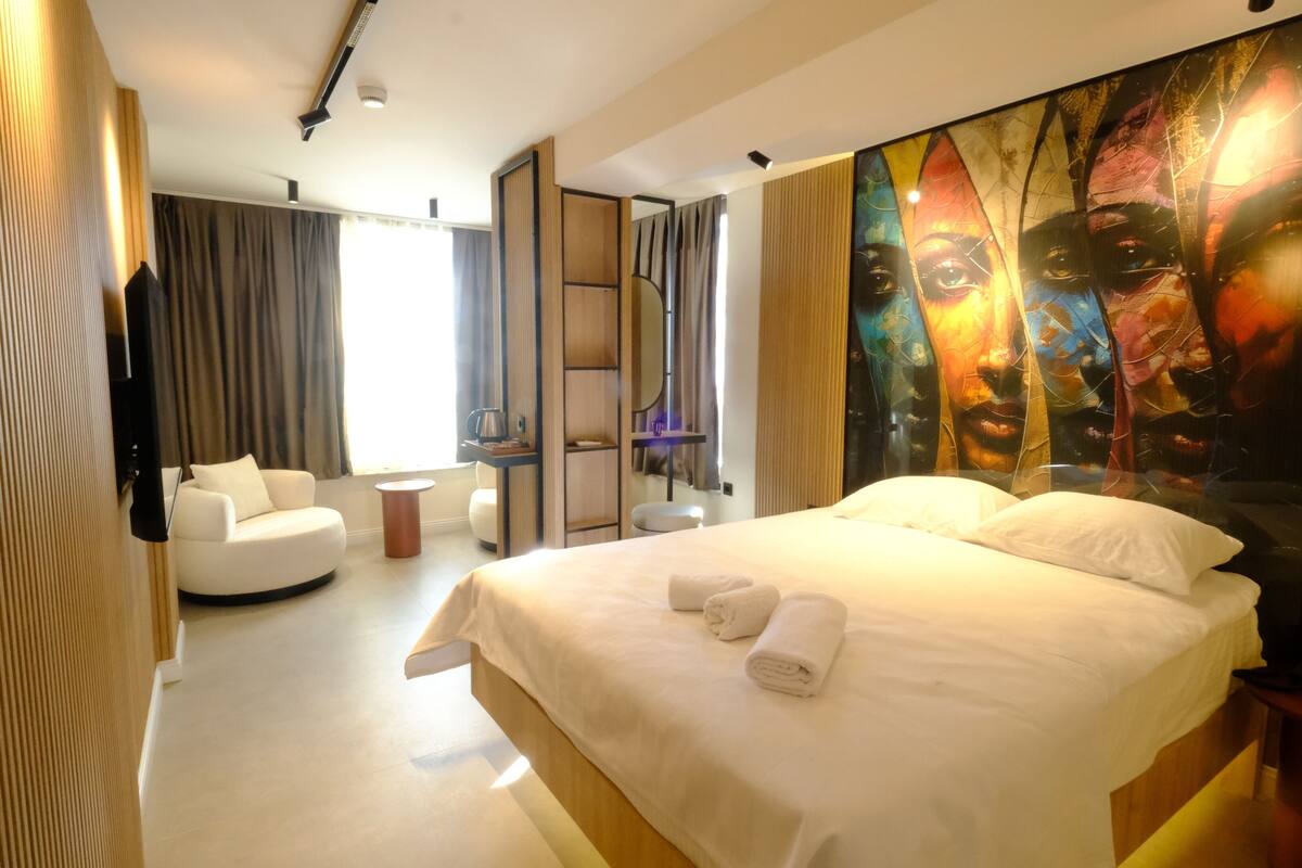 A modern hotel room with a large bed, a seating area, and a large artwork on the wall.