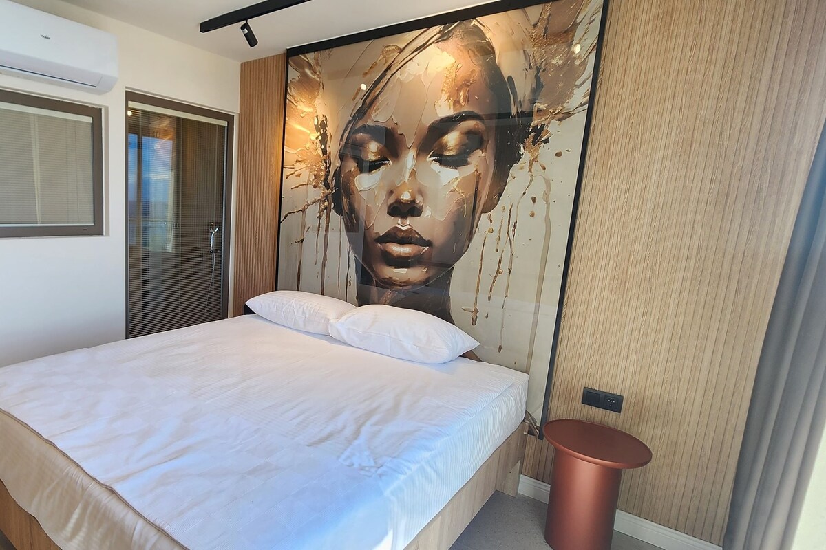 A bedroom with a bed, a wall-mounted air conditioner, a sliding door, and a large abstract painting.