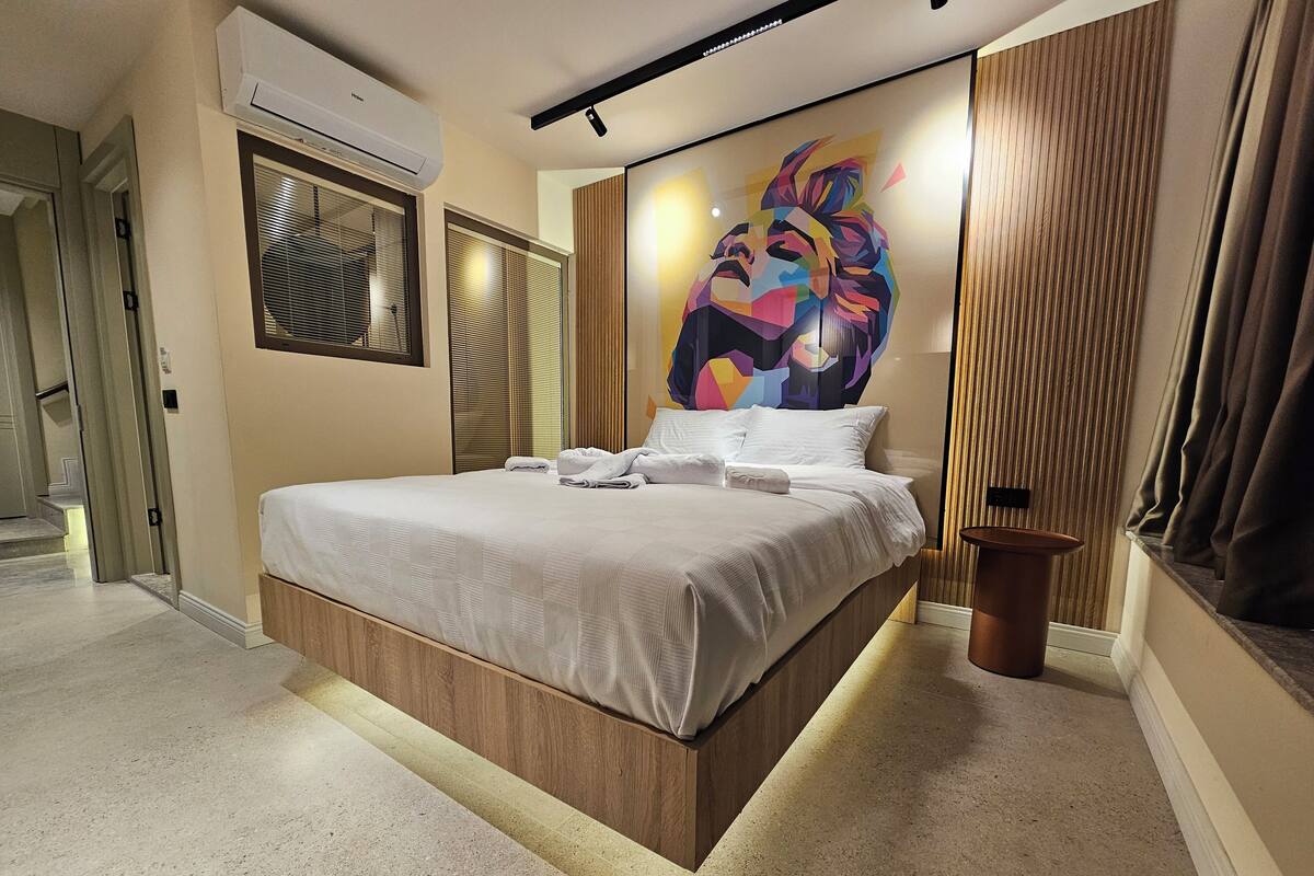 A modern bedroom with a large bed, a wall-mounted air conditioner, and a unique abstract painting.