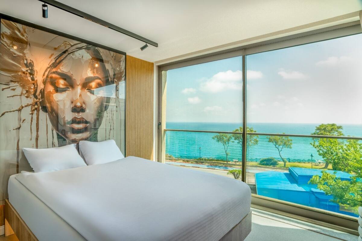 A bedroom with a large bed, a view of the ocean, and a mural on the wall.