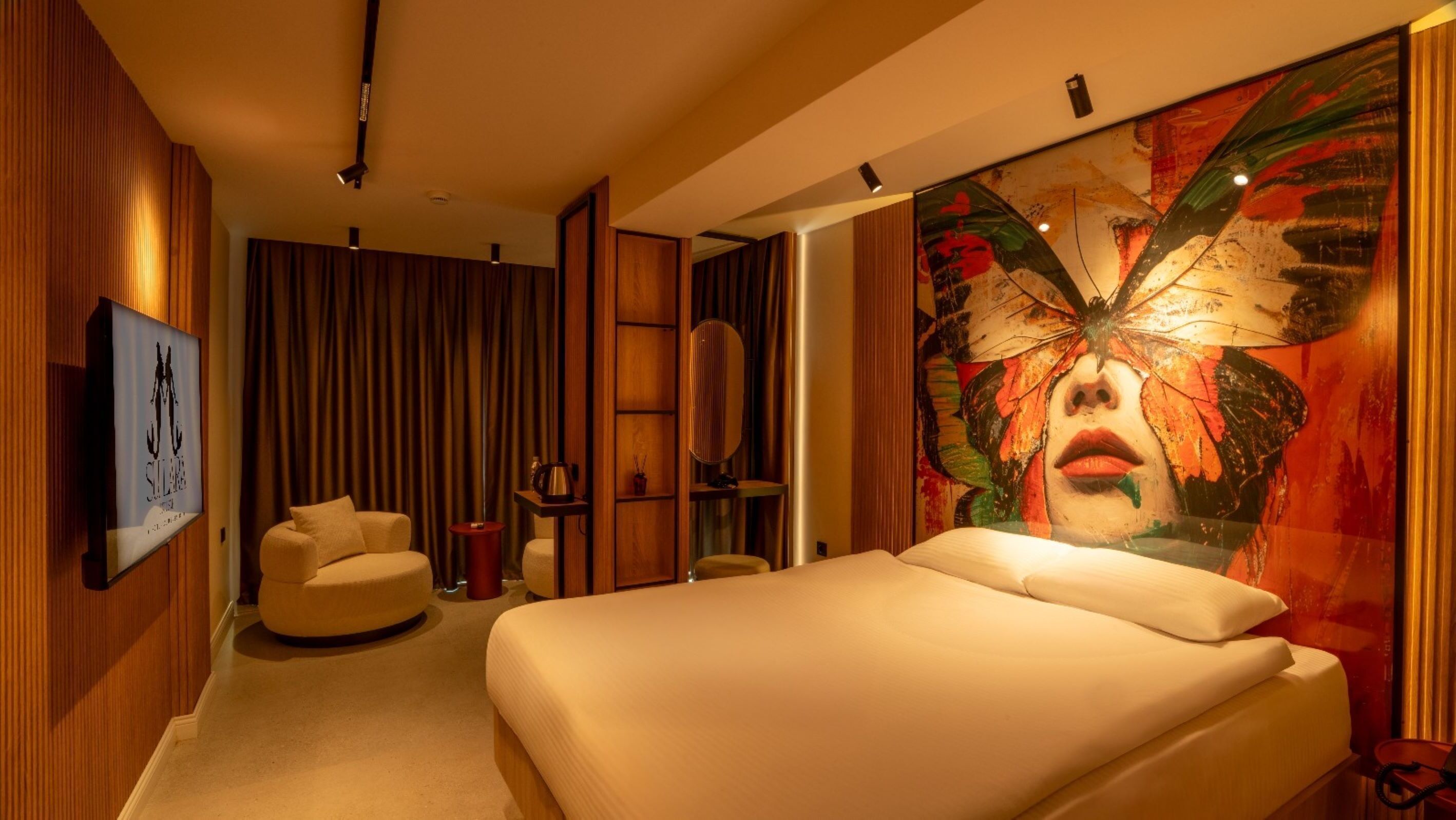 Una habitación de hotel moderna con una cama grande, una zona de estar con sofá, una mesa de centro y un cuadro abstracto de gran tamaño en la pared.