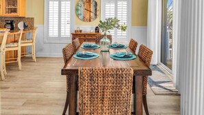A dining area with a wooden table, woven chairs, and a decorative wall clock. - Perfect Timing- On The Beach, Sleeps 10 (Port St. Joe)