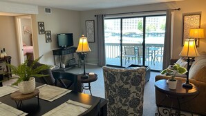 Un salon comprenant un coin repas, un téléviseur et un balcon aménagé avec du mobilier d’extérieur.