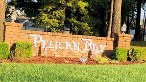Un mur de briques sur lequel on peut lire en grandes lettres le mot « PELICAN BAY », le tout étant entouré d’herbe et de petits arbustes.
