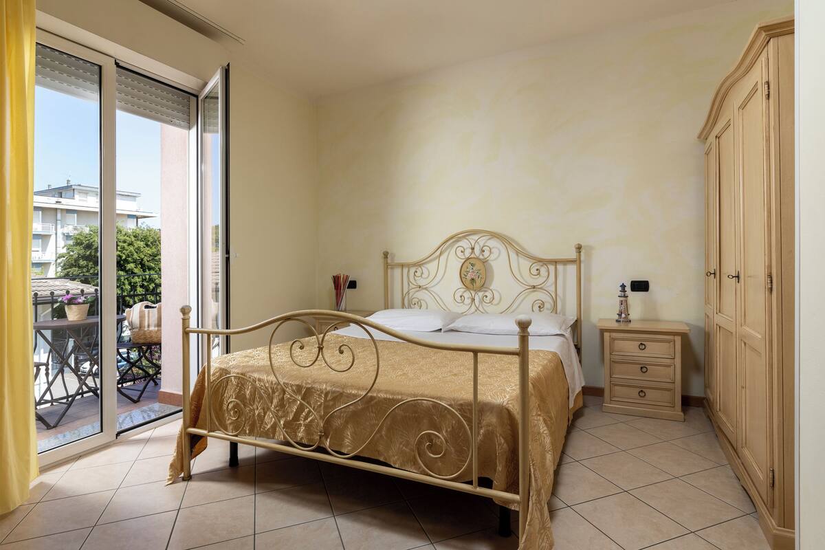 Une chambre à coucher comprenant un lit, une table de chevet, une armoire et une porte-fenêtre coulissante donnant sur un balcon.