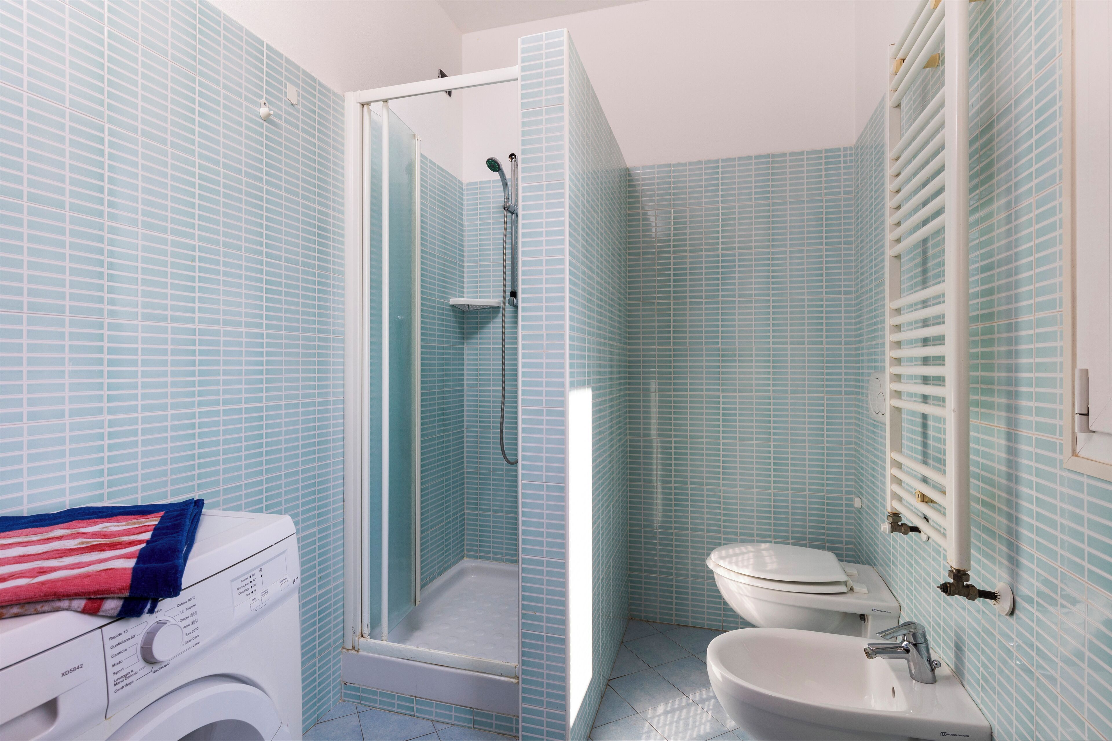 Une salle de bain avec une douche à parois de verre, un lave-linge et un lavabo.