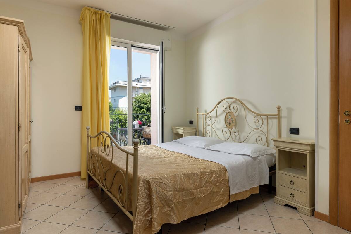 Une chambre à coucher comprenant un lit, une table de chevet, une armoire et une porte-fenêtre coulissante donnant sur l’extérieur.