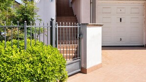 Une entrée fermée par un portail, avec un escalier menant à un garage.
