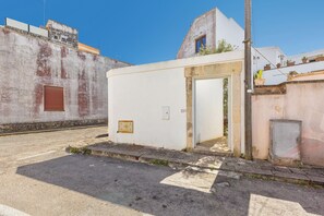 Un piccolo edificio bianco con una sola porta e una piccola finestra, situato all'angolo di una strada sotto un cielo sereno.