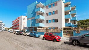 Un edificio residencial de varios pisos con balcones, coches estacionados y una entrada porticada.