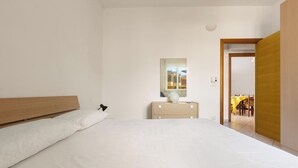 Un dormitorio con cama, cómoda, espejo y puerta que da a un comedor.